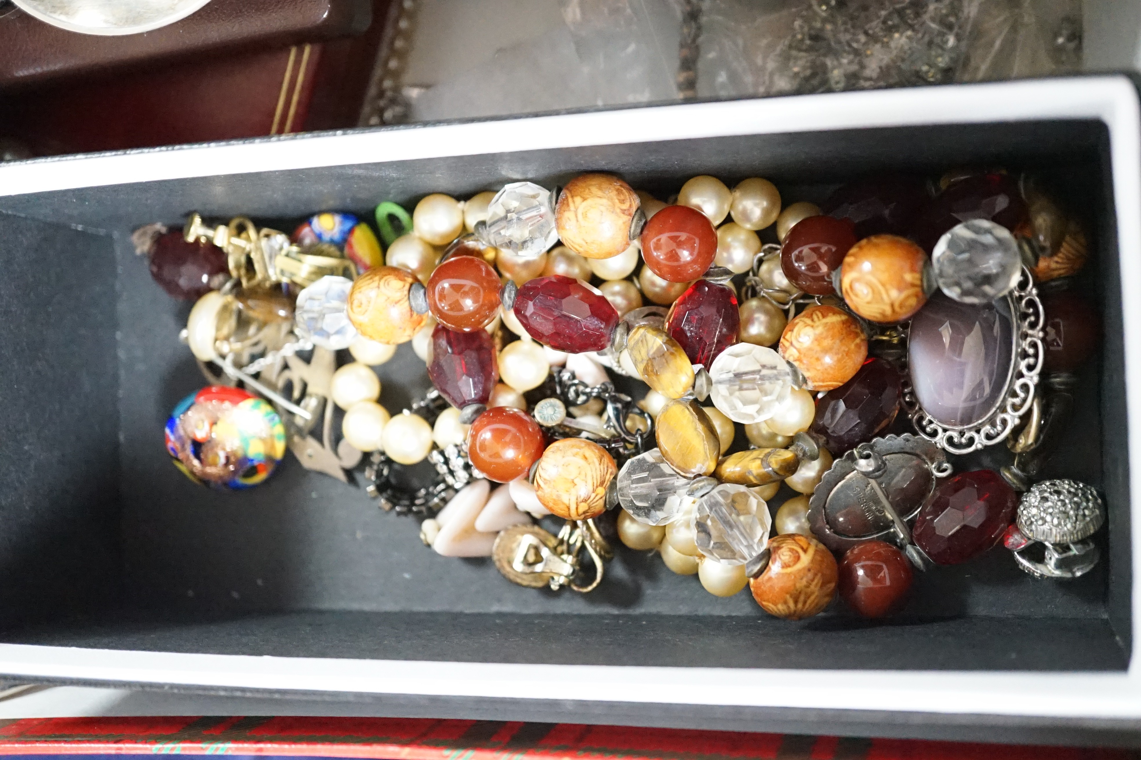 A collection of assorted jewellery including costume, silver and enamel flower head brooch, silver mounted amber cigarette holder, plated flatware, necklaces, commemorative coin, Victorian silver locket, white metal brac